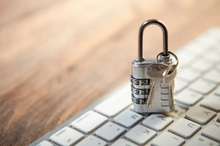 Close up of a padlock sitting on top of a computer keyboard. The lock has a silver key dangling from top, symbolizing security.